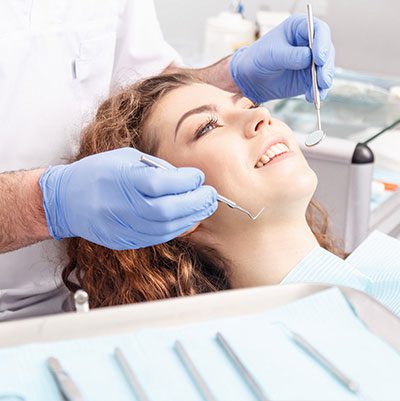 A woman smiles in a dental chair as a dentist with blue rubber gloves prepares to examine the patients mouth