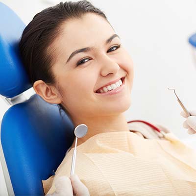 A young patient smiles on a blue dental chair as a dentist prepares to work on her teeth 